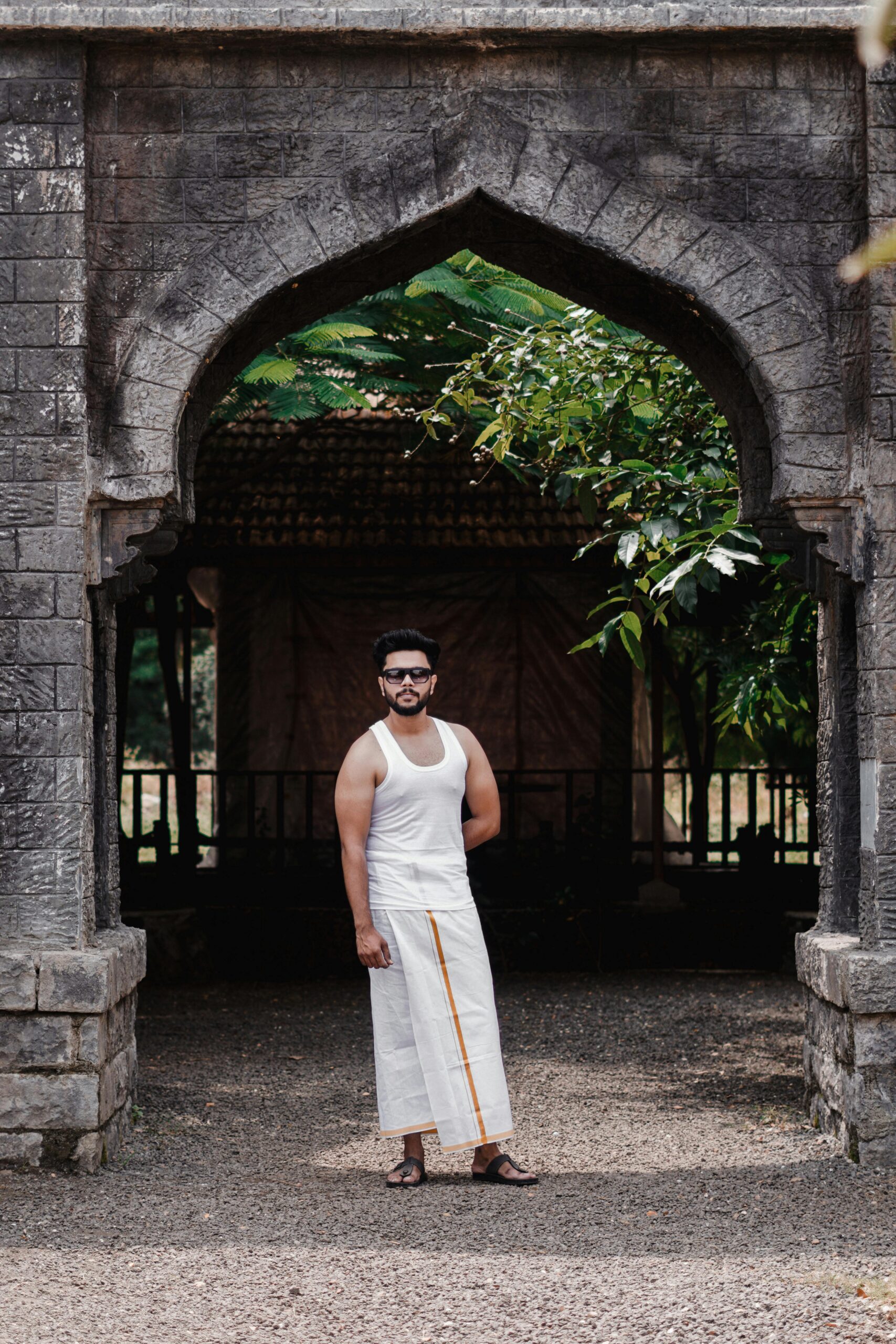 Portrait of an Indian man in traditional attire, standing under an ancient stone archway, India.
